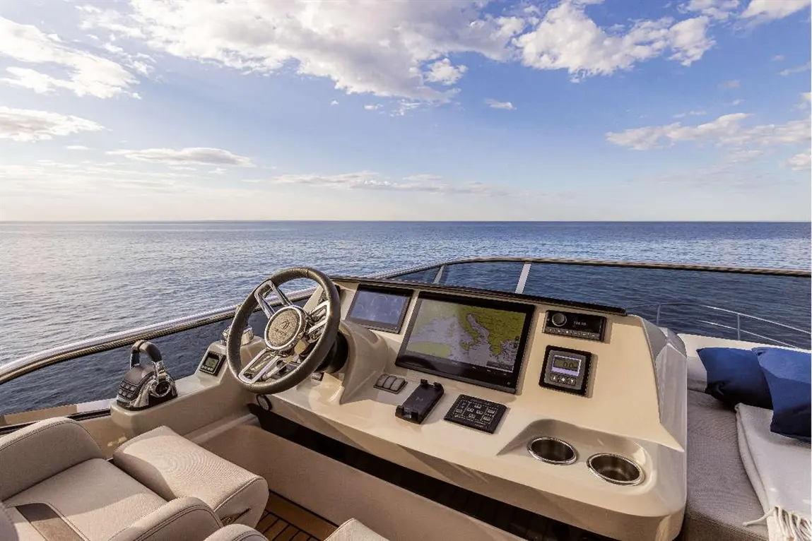 Luxury yacht cockpit featuring a steering wheel, navigation screen, and ocean view under a clear sky.
